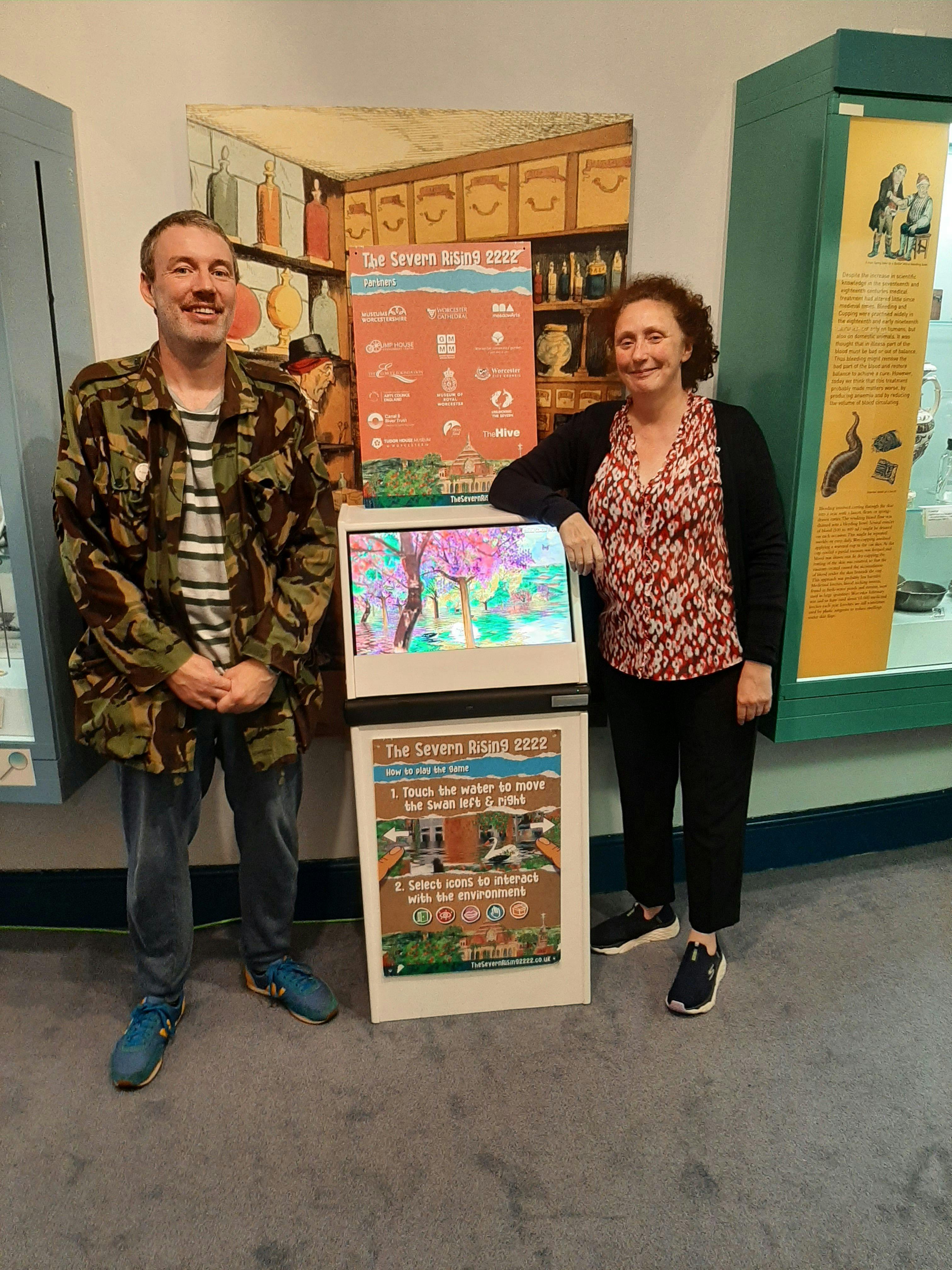 Andy Round and illustrator Sarah Millin stand next to the arcade version of The Severn Rising 2222 at the George Marshall Medical Museum.
